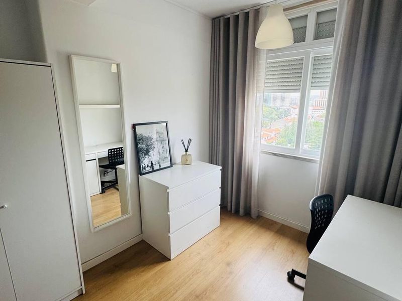 Double bed with a green throw, beside a white three-door wardrobe on wood flooring.