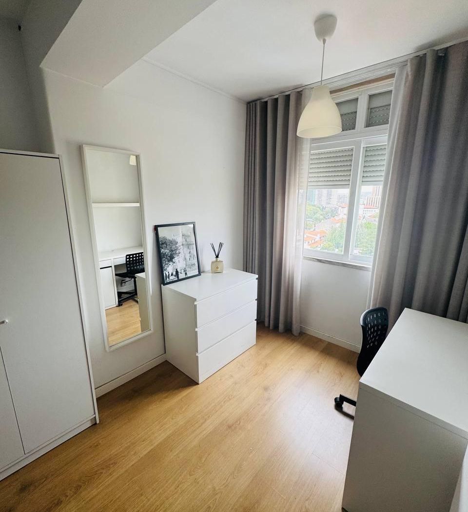 Double bed with a green throw, beside a white three-door wardrobe on wood flooring.