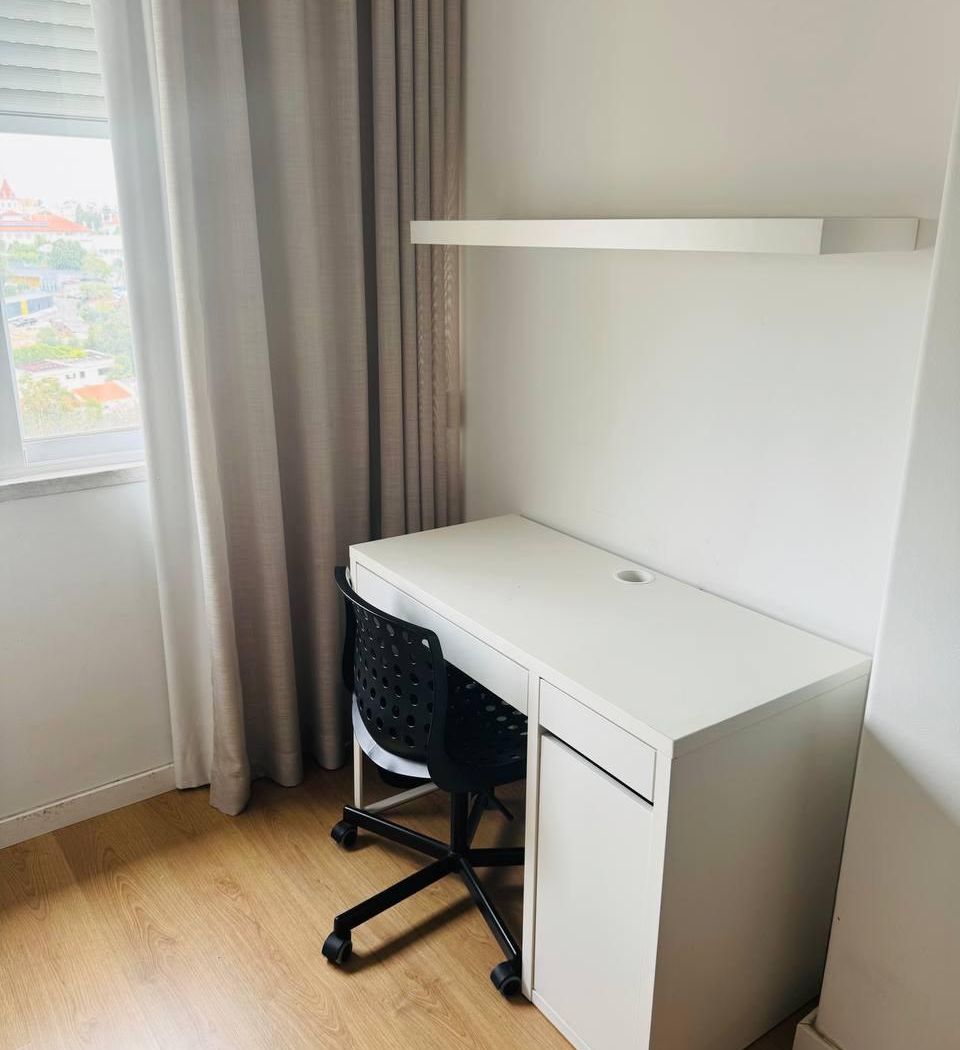 Desk and swivel chair by the window, with a shelf above and a view over the neighbourhood.