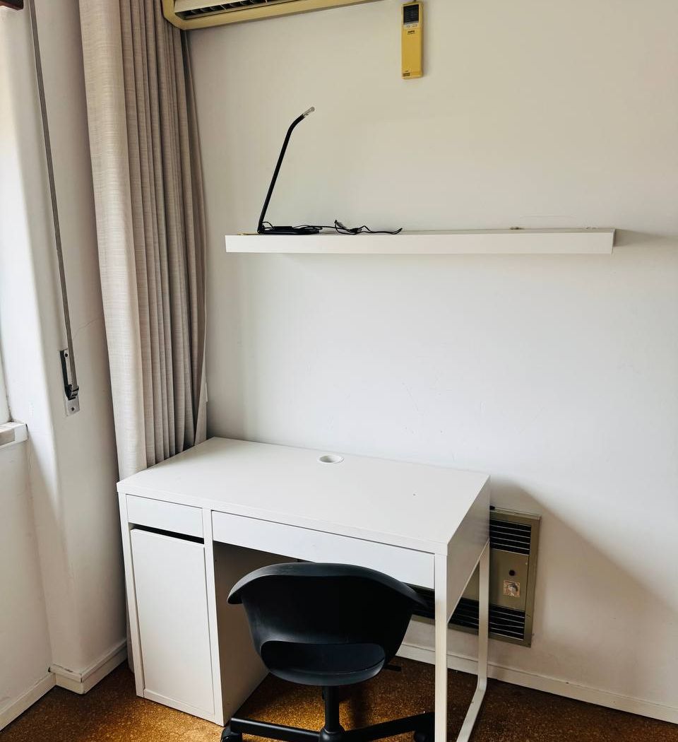 Desk with a reading lamp and a shelf above it, in the corner beside the window.