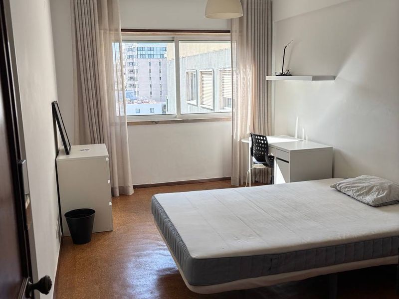 The room from the doorway: double bed, a desk and swivel chair by the window, and a chest of drawers with a mirror against the near wall.