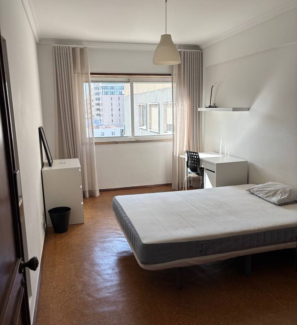 The room from the doorway: double bed, a desk and swivel chair by the window, and a chest of drawers with a mirror against the near wall.