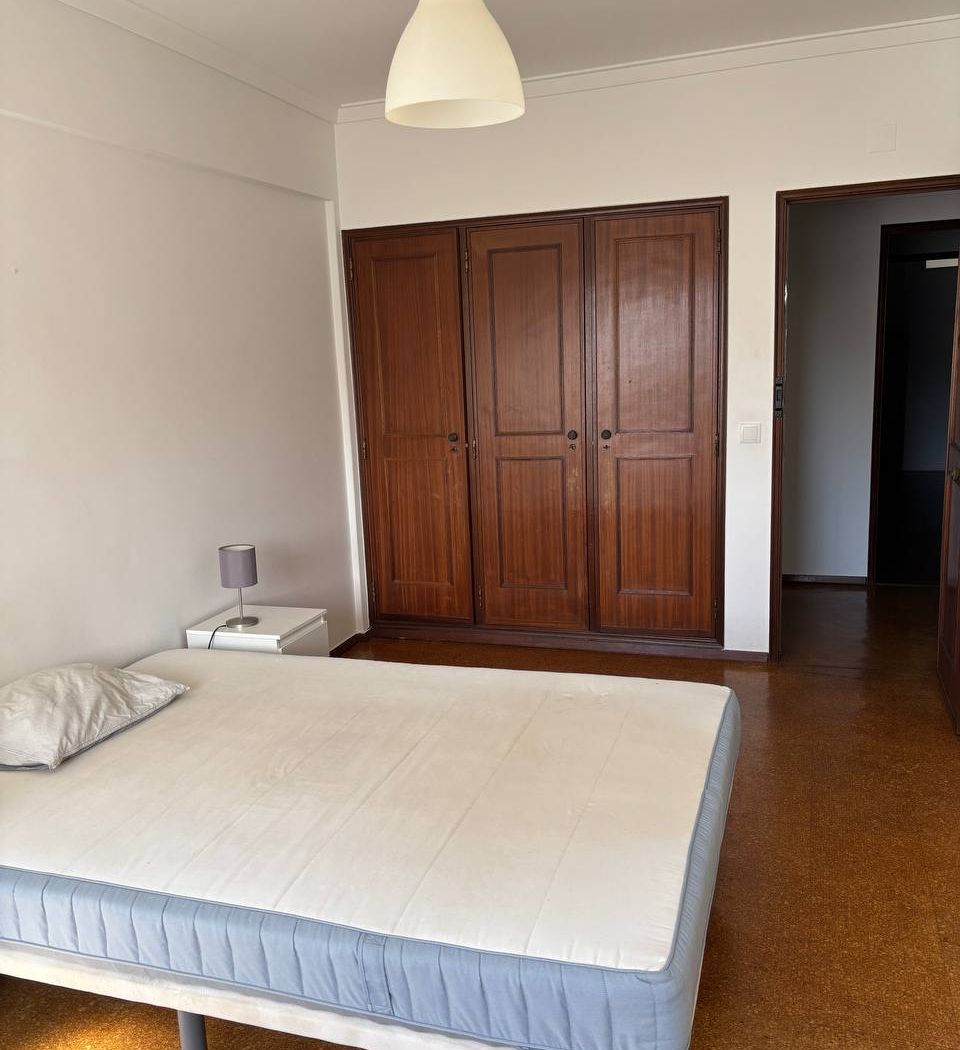 Built-in wardrobe with three dark wood doors, next to the door onto the hallway, with a bedside table and lamp beside the bed.